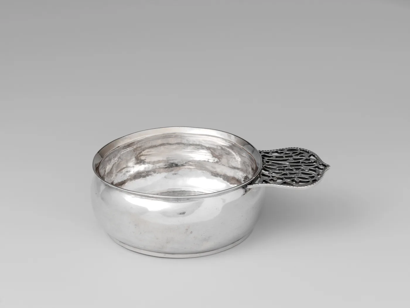 Silver porringer by Andrew Billings of Poughkeepsie New York with dense scrolled openwork filling a leaf shaped handle inside a beaded edge