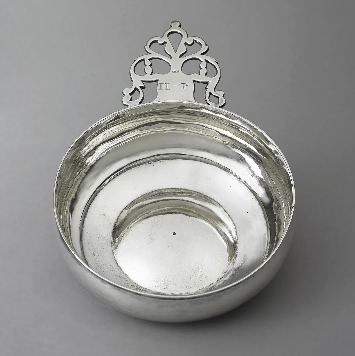 American porringer of about 1740 photographed from directly above, the pierced handle struck HURD in a plain rectangle and engraved with the initials H and P