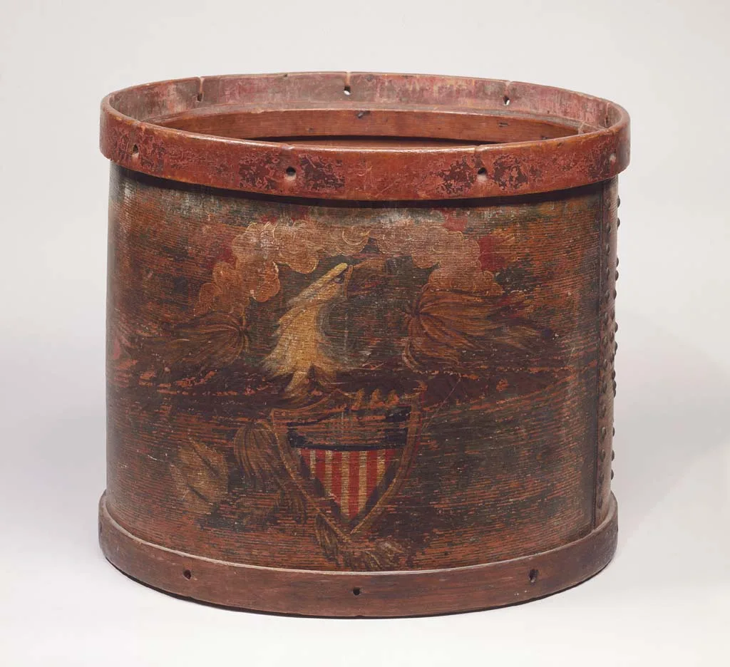 Cylindrical snare drum with a wooden shell painted deep red, decorated with an eagle and a striped shield, its hoops darkened with age