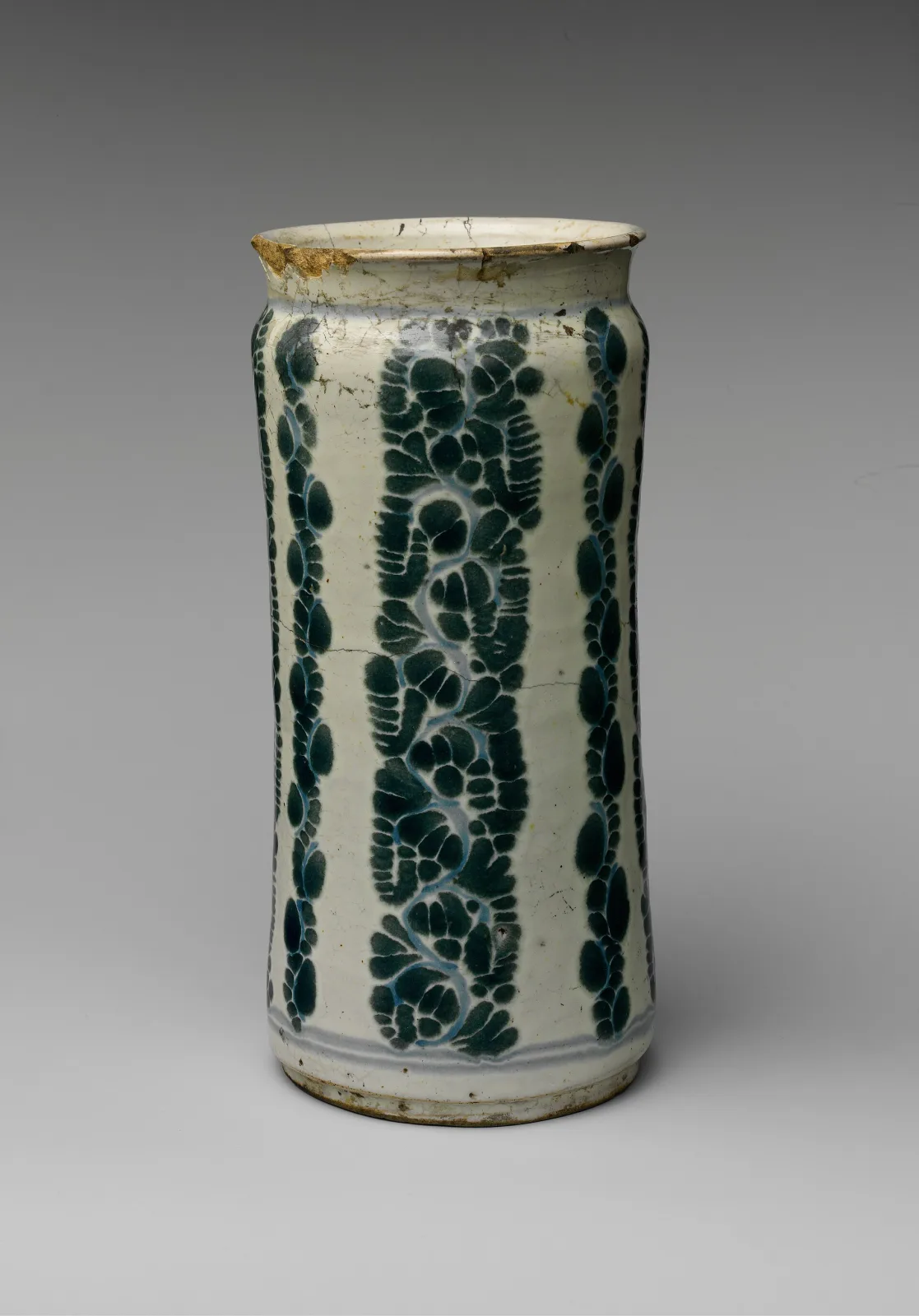 Mexican cylindrical apothecary jar with four vertical bands of stippled green foliage on a cream glaze, a large loss at the rim stained brown, and dark stress cracks running down the wall