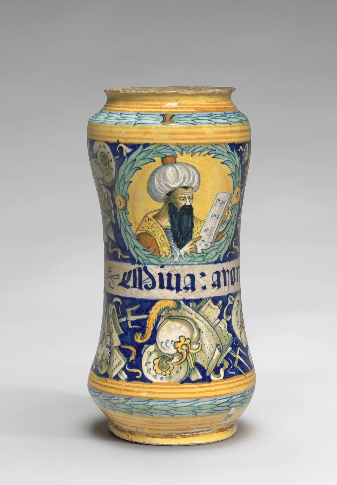 Italian maiolica albarello painted with a turbaned, black-bearded man holding an open book inside a green wreath, above a white band lettered in gothic blackletter