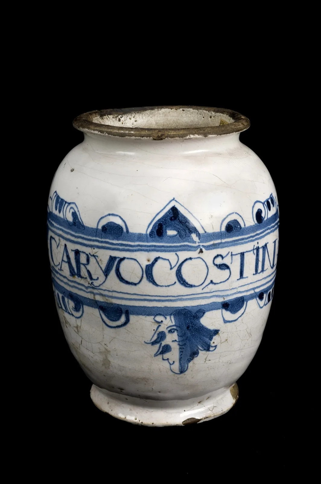 English delftware drug jar painted in blue on white with the word CARYOCOSTIN inside a draped ribbon band, a winged cherub head beneath it, and chipping around the rim
