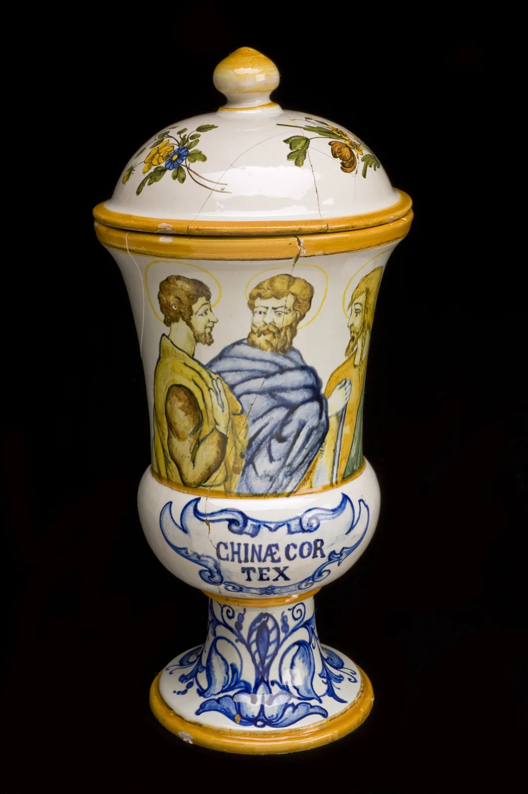 Footed Italian drug jar with a domed cover and knop finial, painted with three haloed figures around the body and the words CHINAE COR TEX on a scrolled band around the pedestal