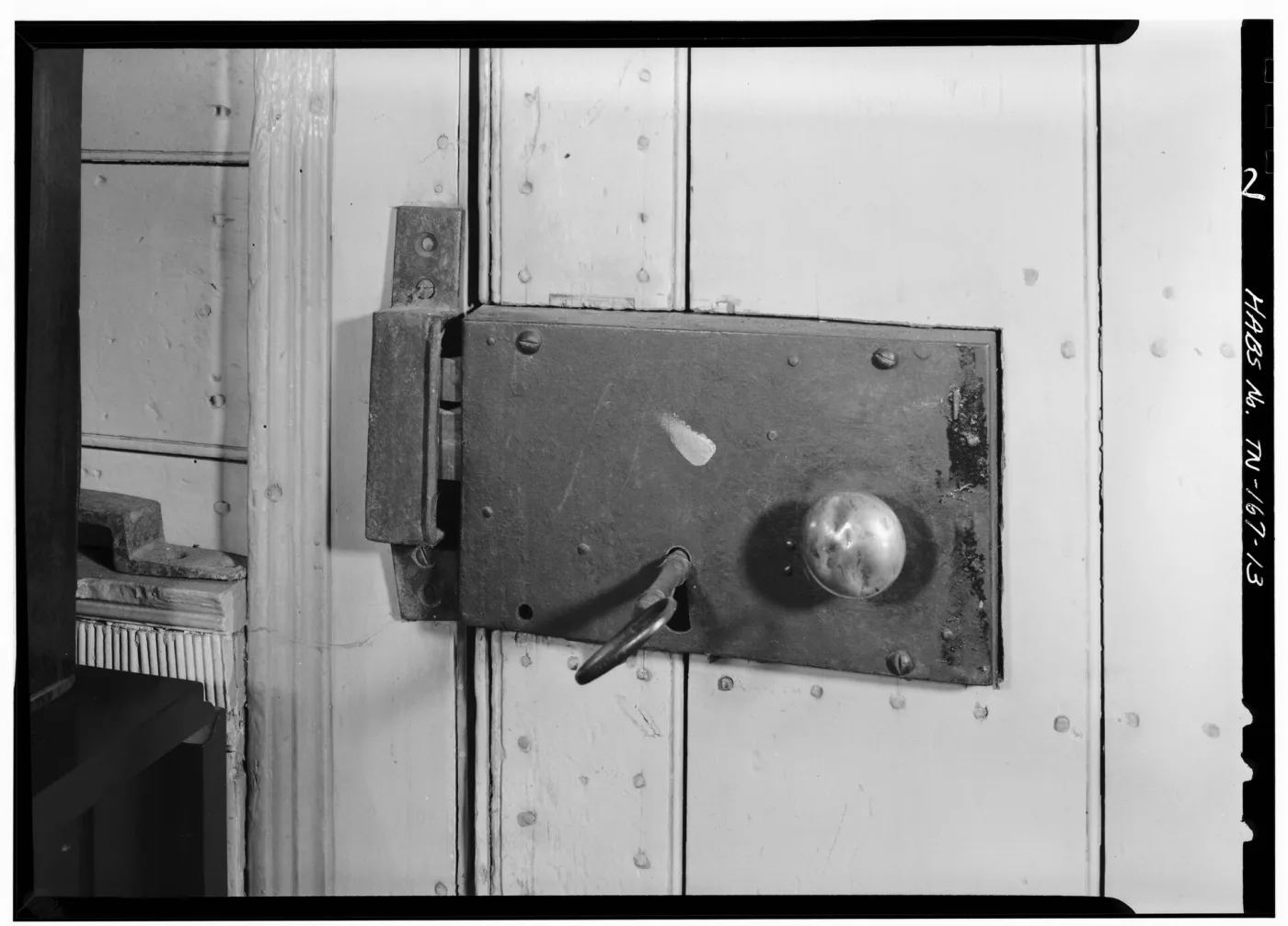 Survey photograph of a cast iron rim lock mounted on the face of a batten door, with a glass knob and a key in the keyhole