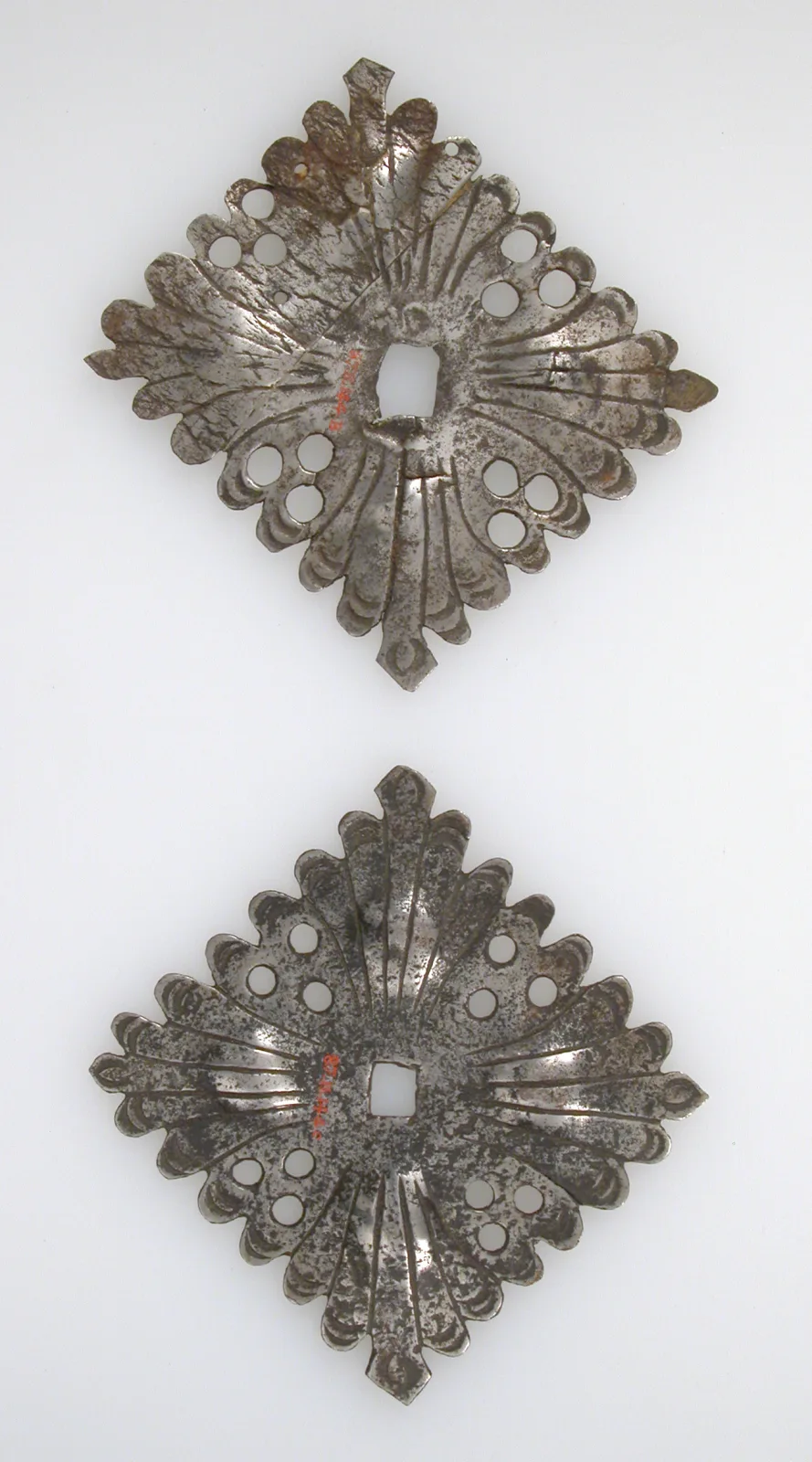 Two diamond-shaped iron escutcheon plates, pierced and chiselled with lobed scalloped edges, shown one above the other
