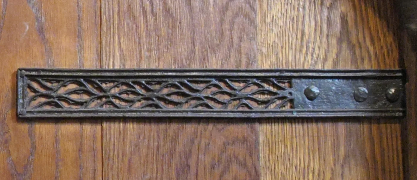 Long wrought iron strap hinge with a pierced band of interlaced scrollwork, mounted on an oak door
