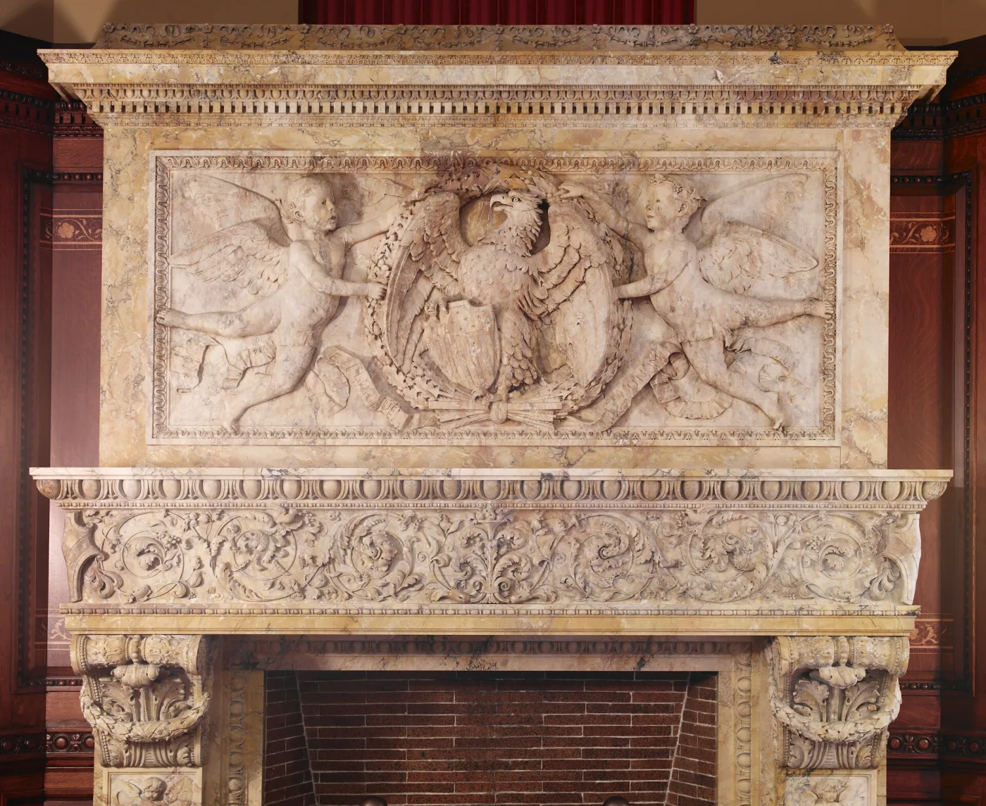 Carved Siena marble mantel with a sculpted frieze of cherubs flanking a central medallion, on carved console brackets