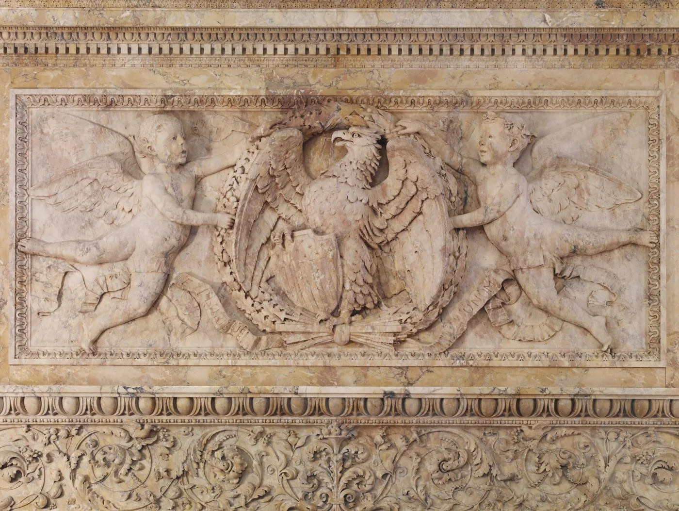 Detail of a carved marble frieze showing an eagle with arrows and a shield, supported by two winged cherubs
