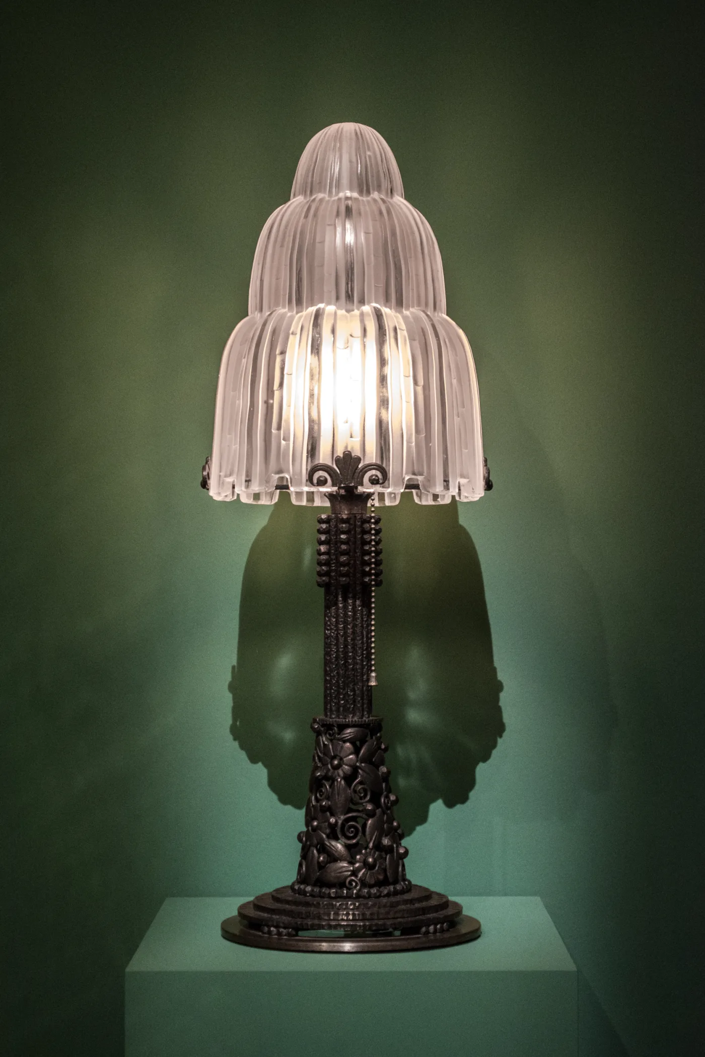 Lit table lamp with a tiered frosted glass shade moulded to look like falling water, on a wrought iron stem with forged flowers and a stepped foot