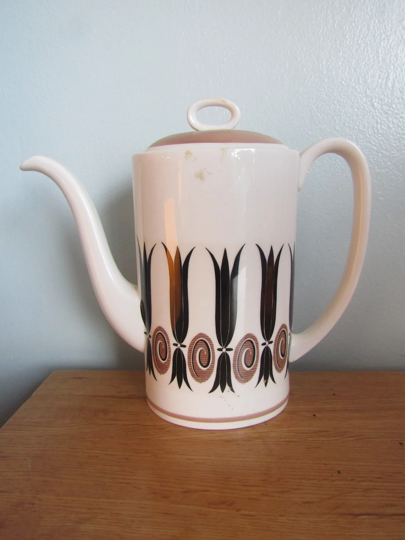 Tall pink coffee pot with a slender curved spout and a black and gold geometric band around the lower body