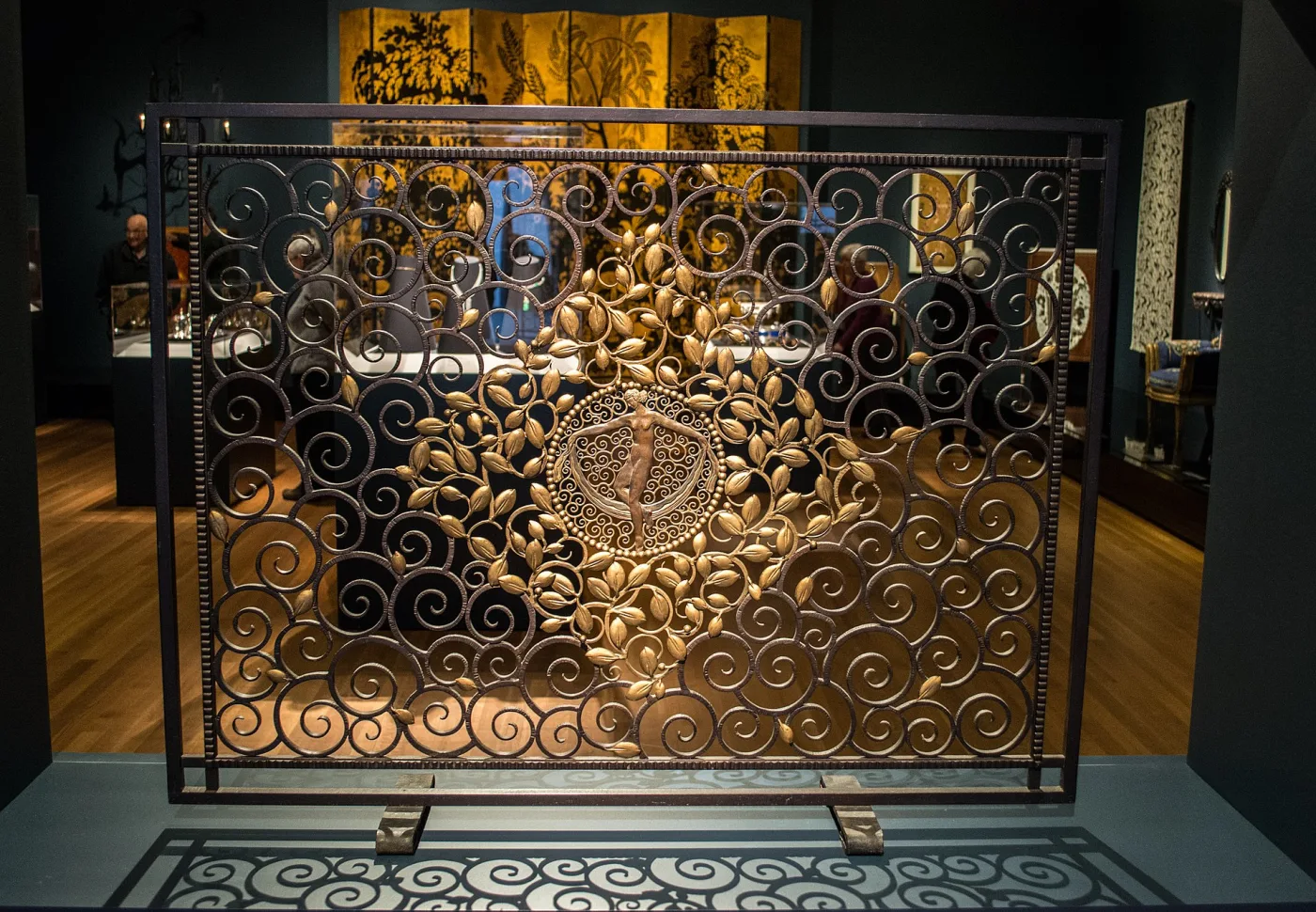 Large rectangular wrought iron fire screen filled with rows of spirals around a gilded central medallion of a standing nude figure