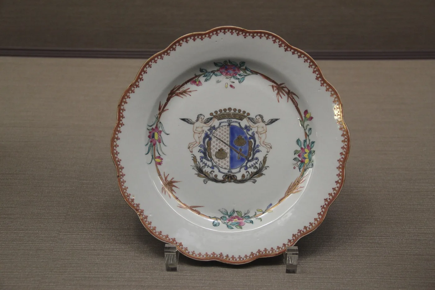 Shallow porcelain plate with a scalloped gilt-edged rim, painted with scattered flower sprays and a central European coat of arms in a shield