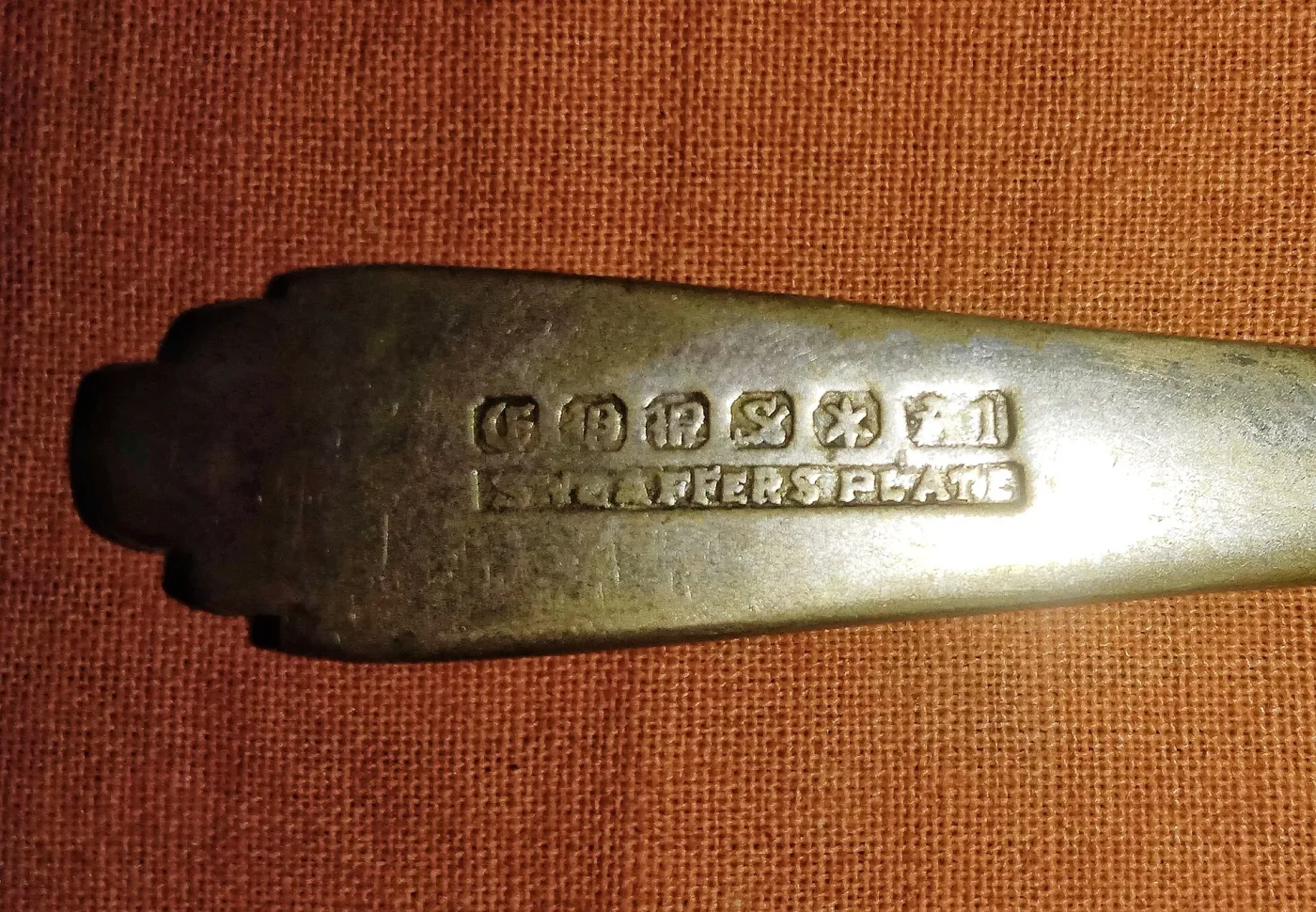Close-up of the back of a tarnished silver spoon stem, showing a row of small struck marks in a shallow line