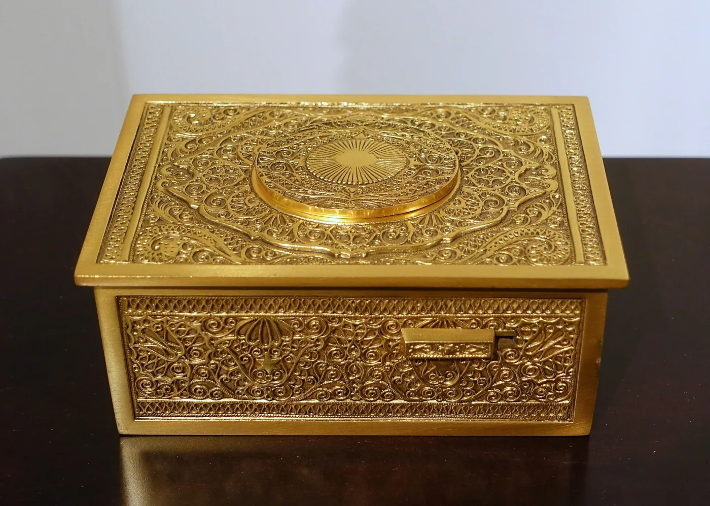 Rectangular gilt box with an all-over engraved and pierced surface and a small oval grille in the lid, standing closed on a dark table