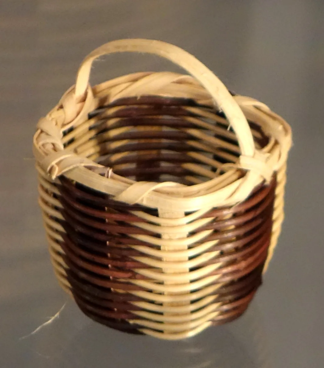 Small round basket woven from narrow splints in alternating bands of natural, dark brown and pale green, with two arched handles at the rim