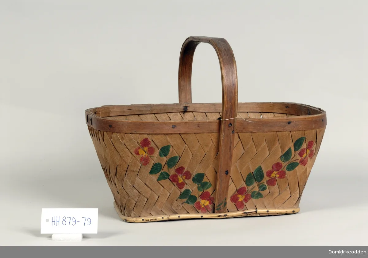Oval basket made from broad flat wood chips with a bentwood handle, painted with small red and blue flowers on the pale surface