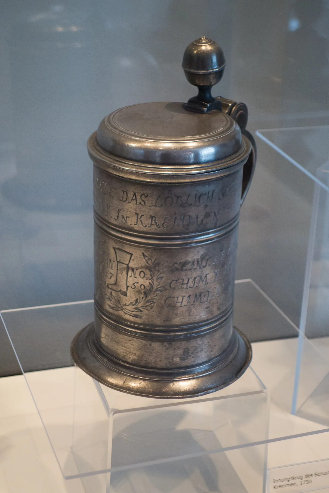Silver beer stein of 1750 with a hinged lid and engraved decoration, displayed in a case
