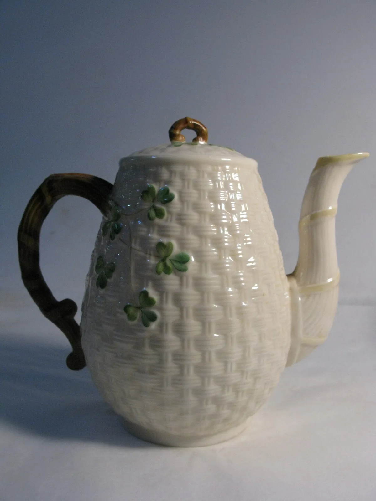 Tall porcelain coffee pot with a moulded basket-weave body, applied green shamrocks and a naturalistic twig handle and finial
