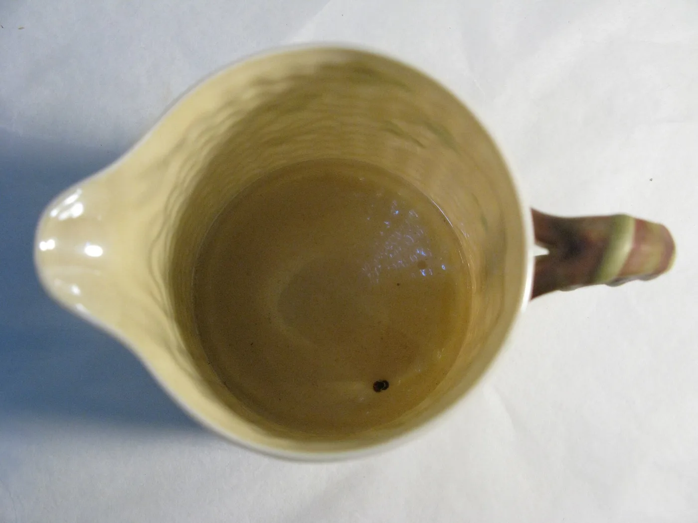 Looking down into the mouth of the milk jug, the inside glazed a soft cream-yellow that catches the light with a faint sheen against the white exterior