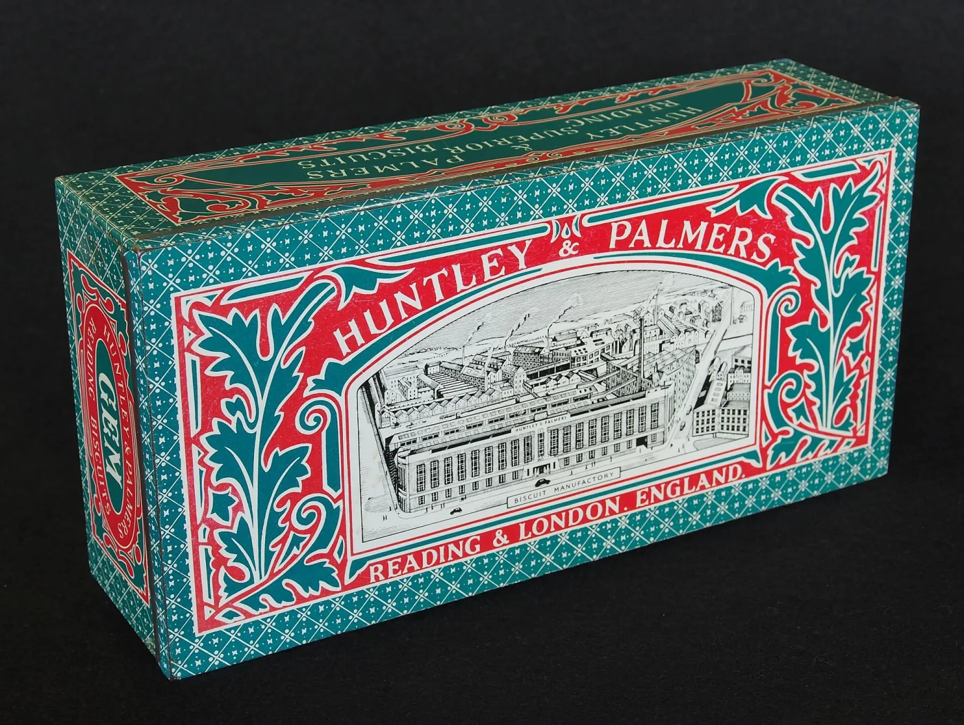 A rectangular biscuit tin printed in red, teal and white with dense foliate borders and a fine engraved bird's-eye view of a large factory