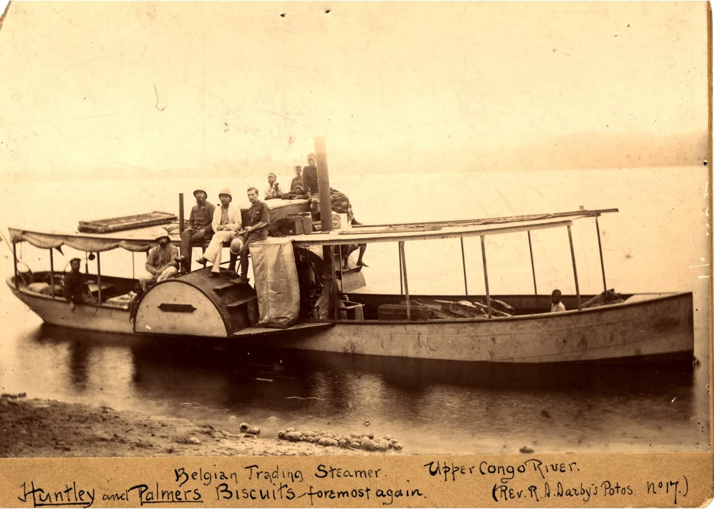 A late nineteenth-century photograph of a small trading steamer on a wide river, with a biscuit tin visible on deck beside the funnel