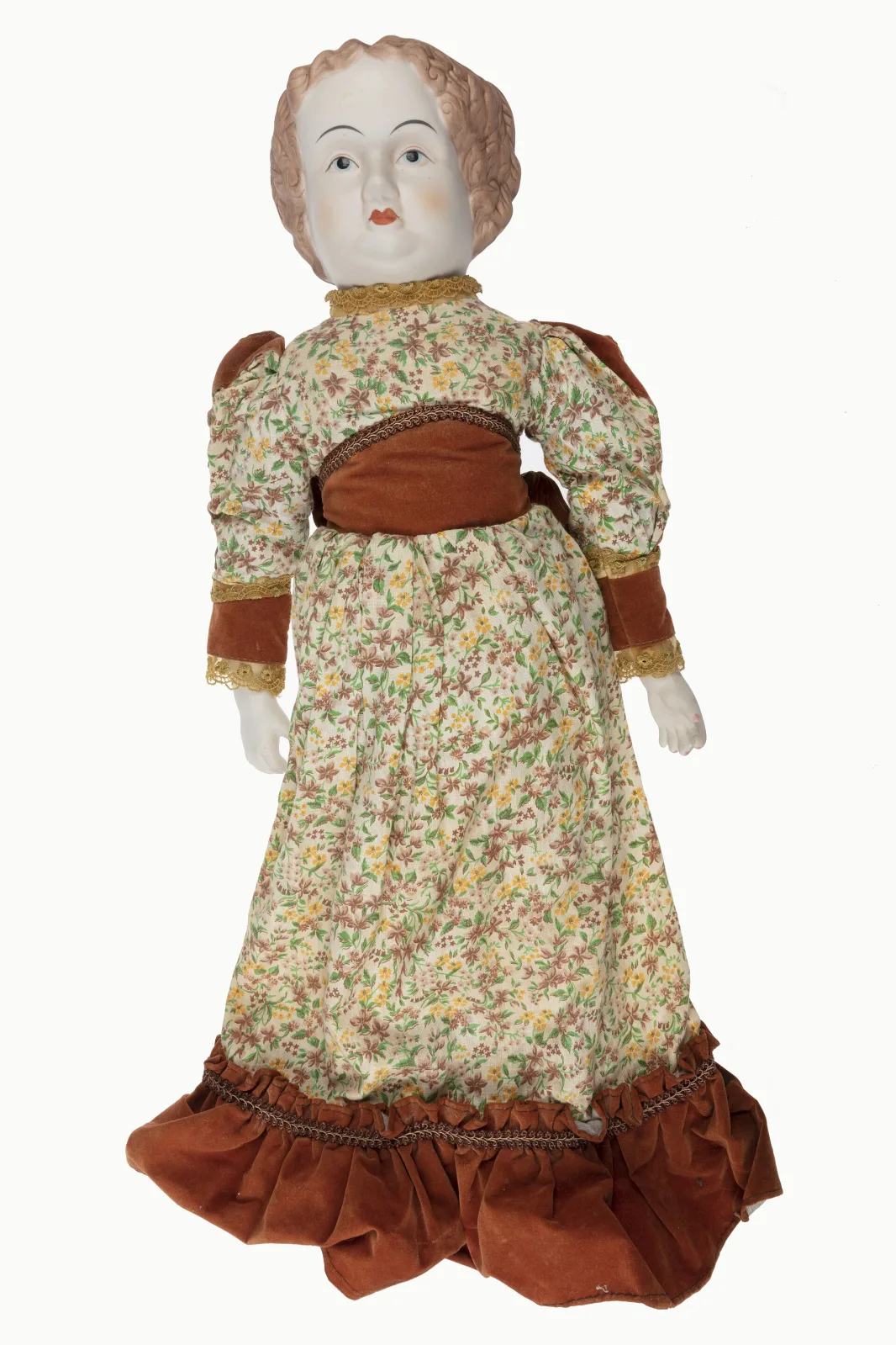 Large doll with a bisque head and bisque hands, dressed in a full-length floral gown with a velvet bodice and trim, standing against a plain background