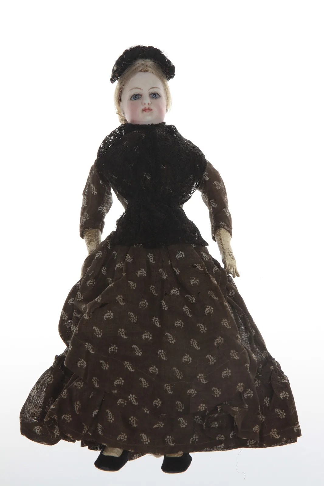 Doll with a pale bisque head and painted features, dressed in a fitted brown and white paisley gown with a full skirt, standing against a plain background