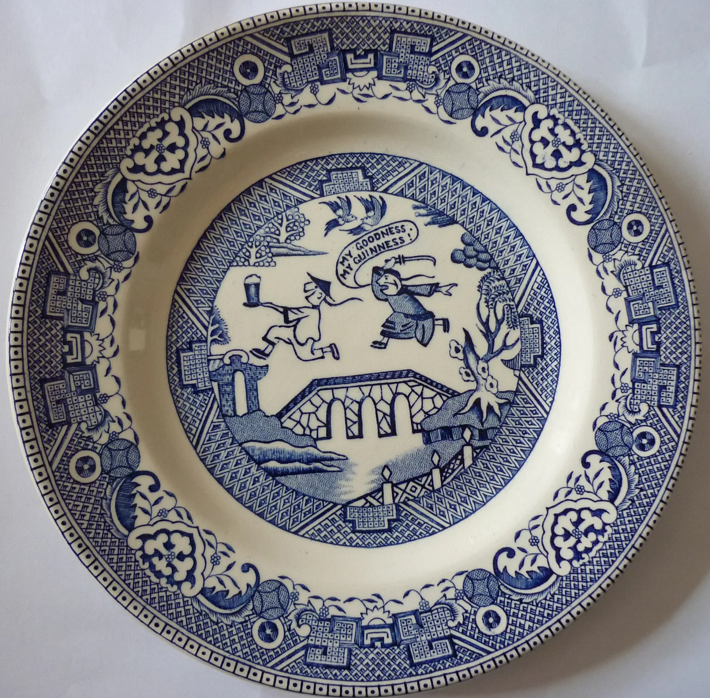 Blue and white plate with an orthodox Willow border of fretwork and scrolled reserves, but a comic centre scene advertising Guinness