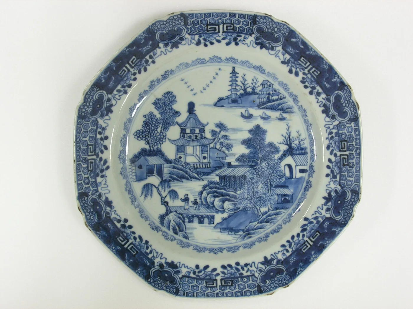 Faceted Chinese porcelain plate hand-painted in blue with a pagoda, a lake with small boats, a bridge and figures