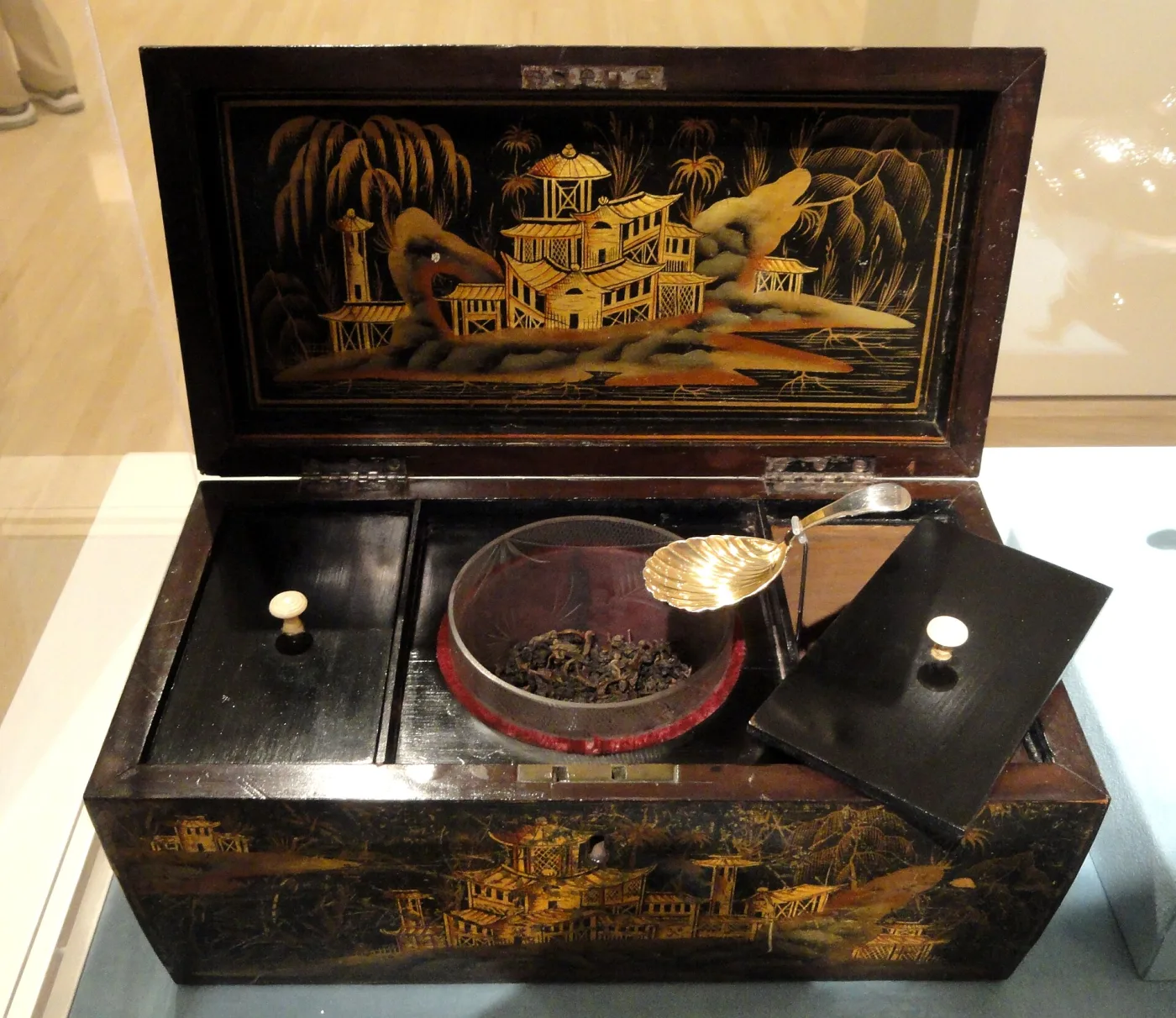Black lacquer tea caddy standing open, its interior divided into two lidded compartments flanking a cut-glass mixing bowl, with a small silver caddy spoon resting beside it