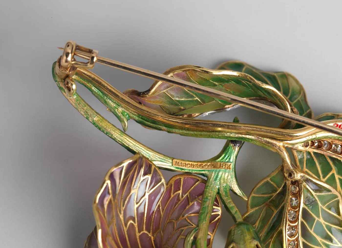 Close-up of the back of an enamelled gold brooch showing the pin stem, tube hinge and catch, with MARCUS & CO and 18K stamped into the gold stem