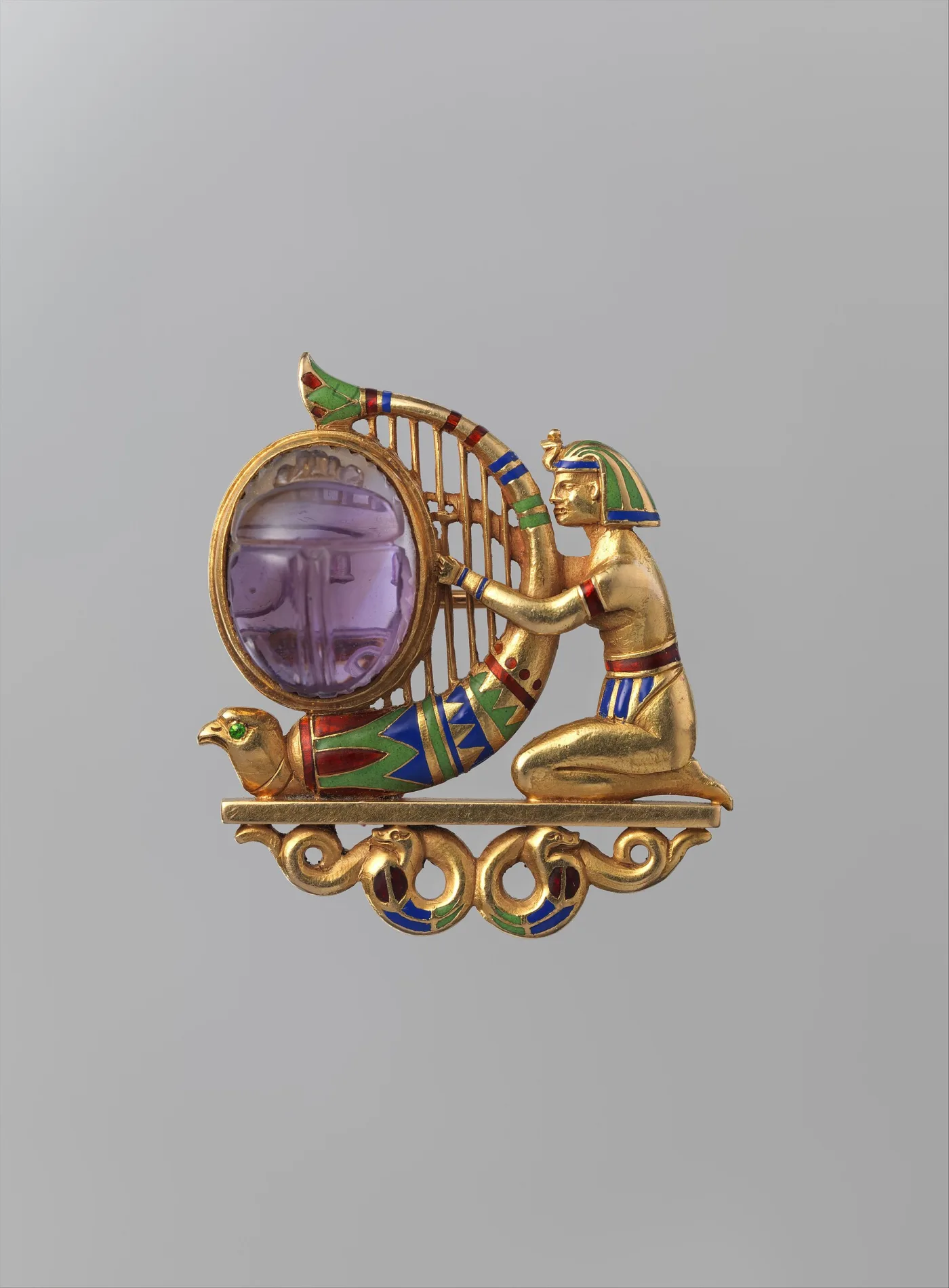 Gold brooch of a kneeling Egyptian harpist in striped blue, green and red enamel, playing a harp whose pillar ends in a falcon head, beside a large purple scarab