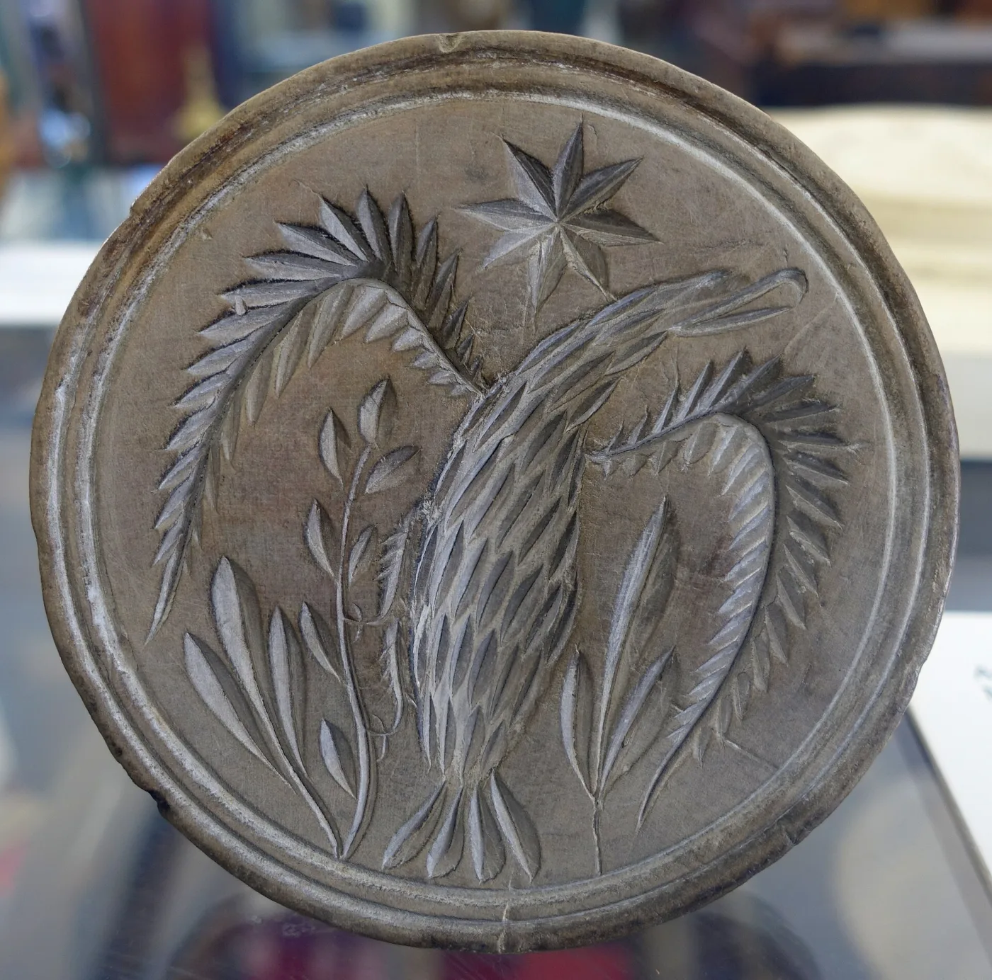 Large round wooden butter print deeply carved with a curved sheaf of wheat and a six-pointed star, the raised edges worn pale and smooth