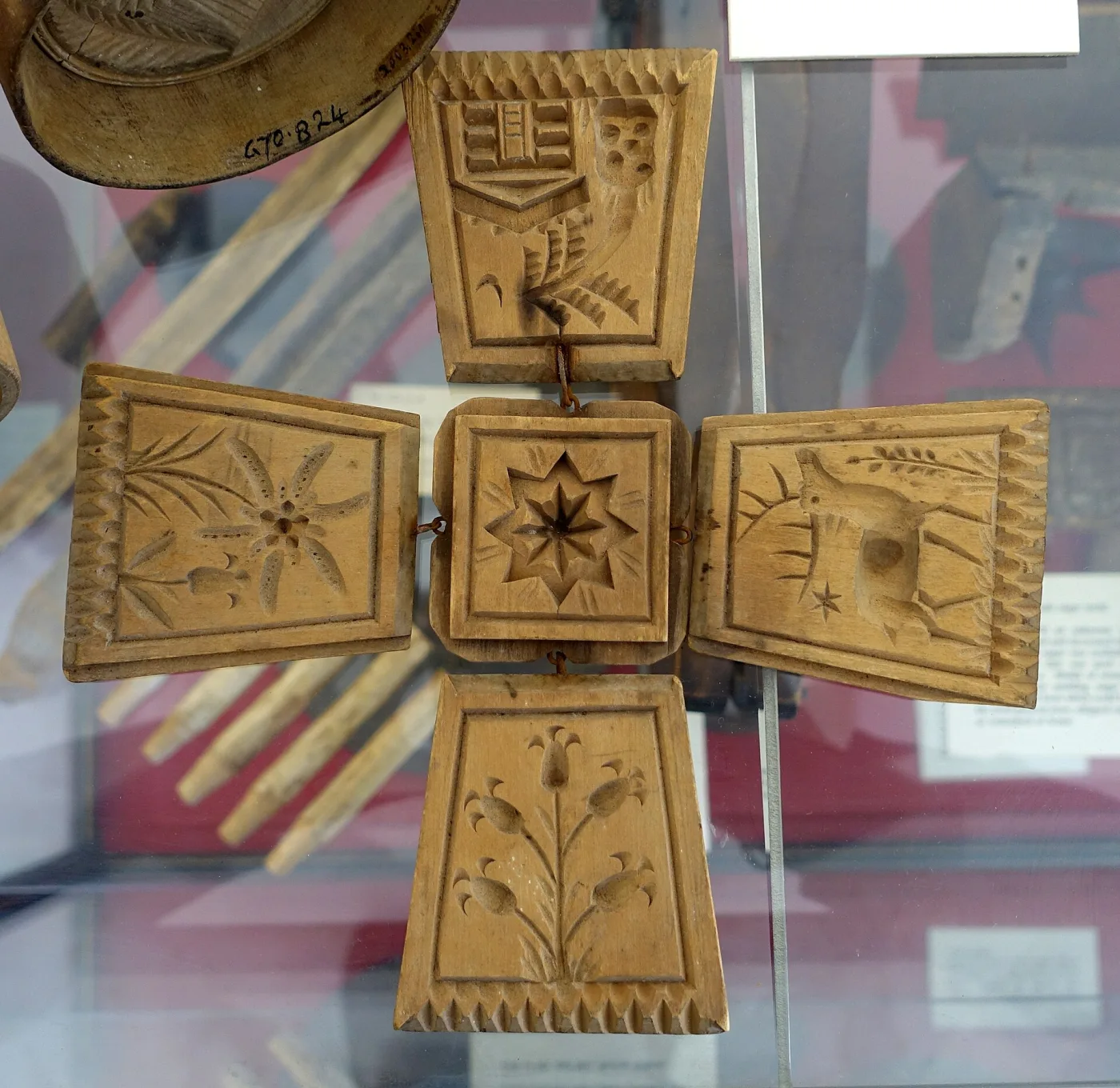 Hand-carved wooden butter mold hinged open into a cross shape, its five square panels each carved with a different design including a shield, a star and flowering plants