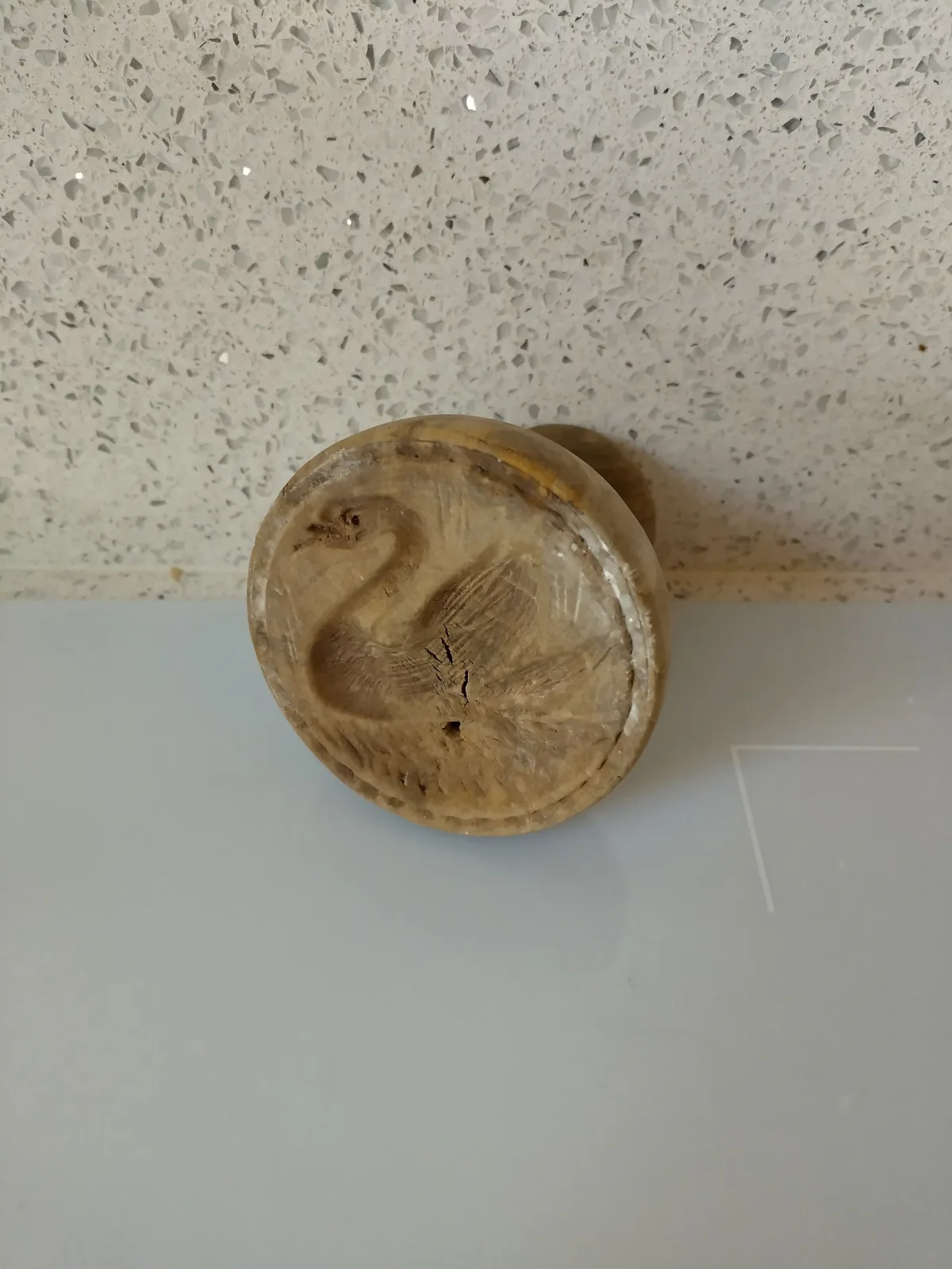 Small round wooden butter stamp resting on its side, its face carved with a swan in low relief