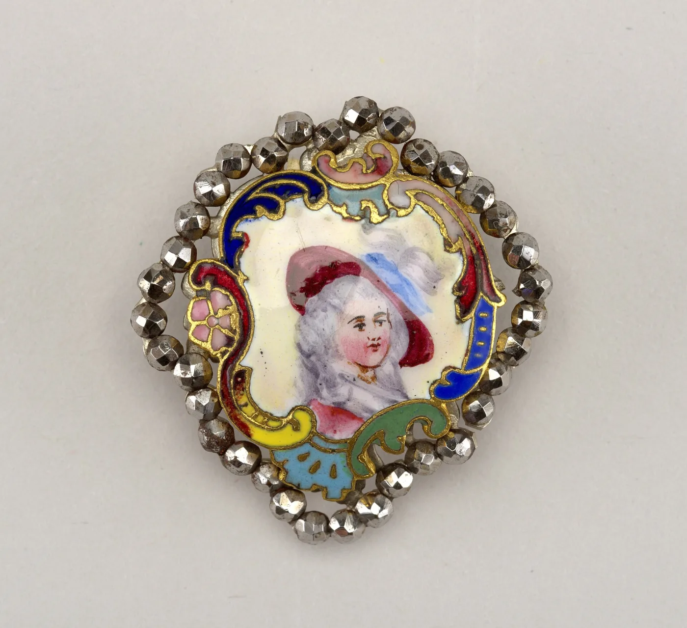 Small 18th-century button with a painted enamel portrait of a woman in a wide plumed hat, set in a shaped rococo cartouche of blue, red and yellow enamel and ringed by faceted cut-steel studs