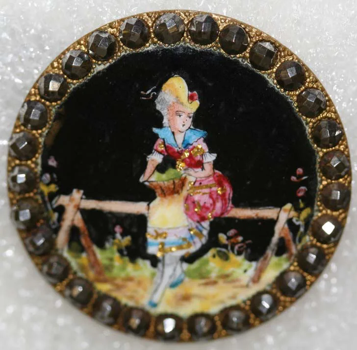 Button with a hand-painted scene of a young woman in a wide hat leaning on a rail against a dark ground, enclosed by a border of faceted cut-steel studs in a gilt setting
