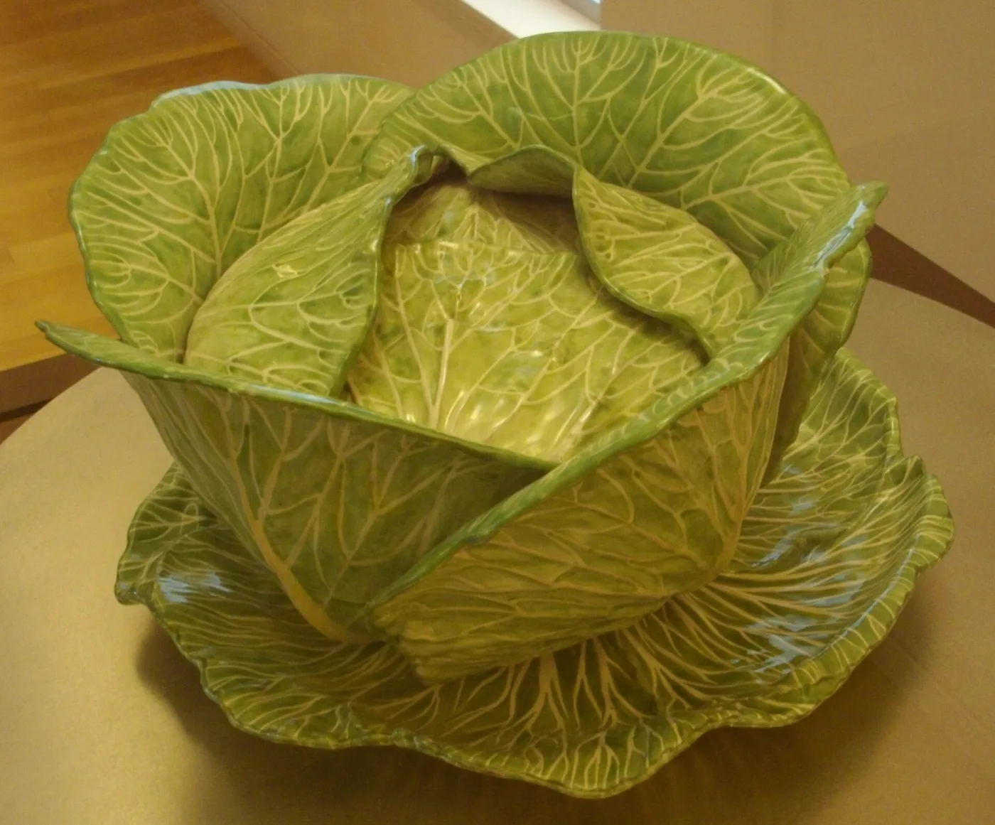 Green faience cabbage tureen with its lid closed, sitting on a matching leaf-shaped stand