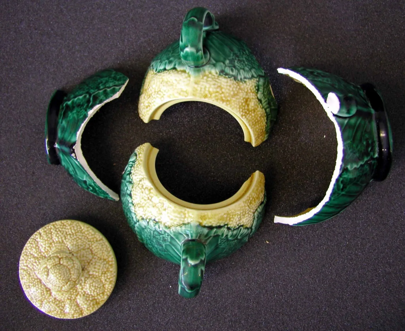 Broken green and cream cauliflower-pattern sugar bowl in four pieces with its lid, the pale body visible along every break edge