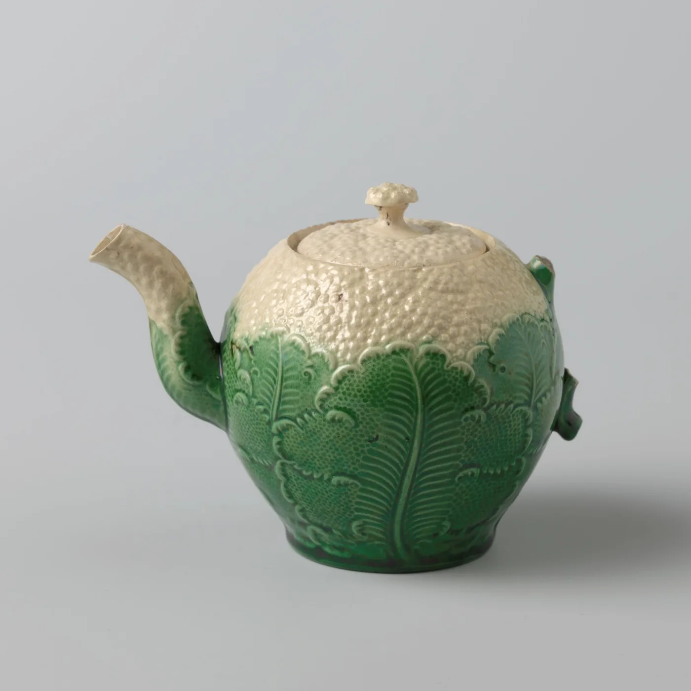 Globular teapot with green moulded leaves below and a stippled cream cauliflower head above, with a curved spout