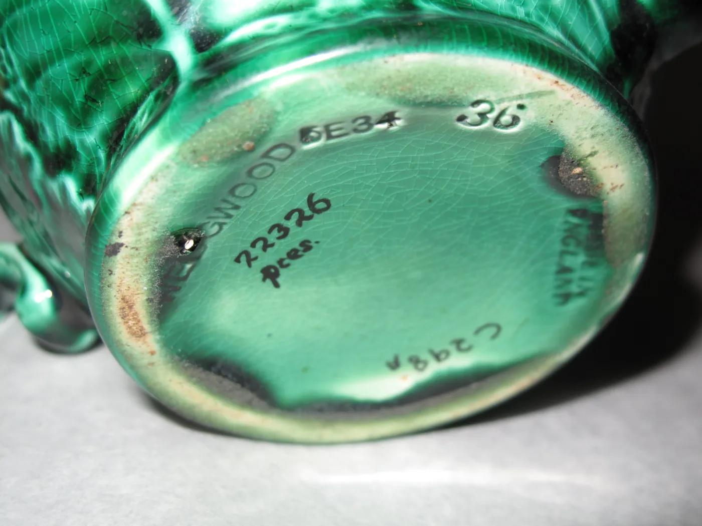Underside of a green-glazed teapot showing the impressed word WEDGWOOD, MADE IN ENGLAND around the rim, and painted numbers
