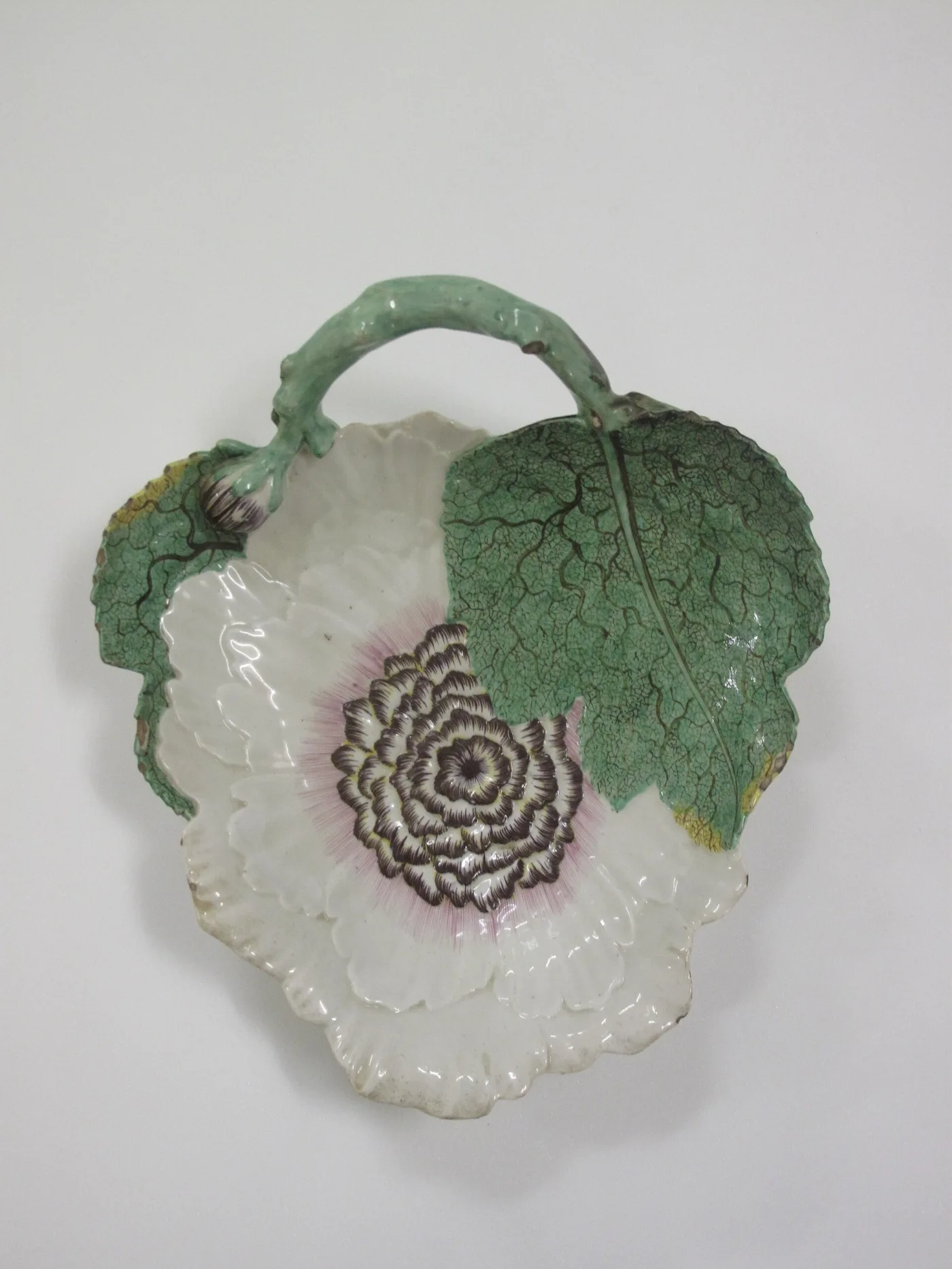 Leaf-shaped porcelain dessert dish with a green cabbage leaf, a white bloom painted in purple, and a twig handle