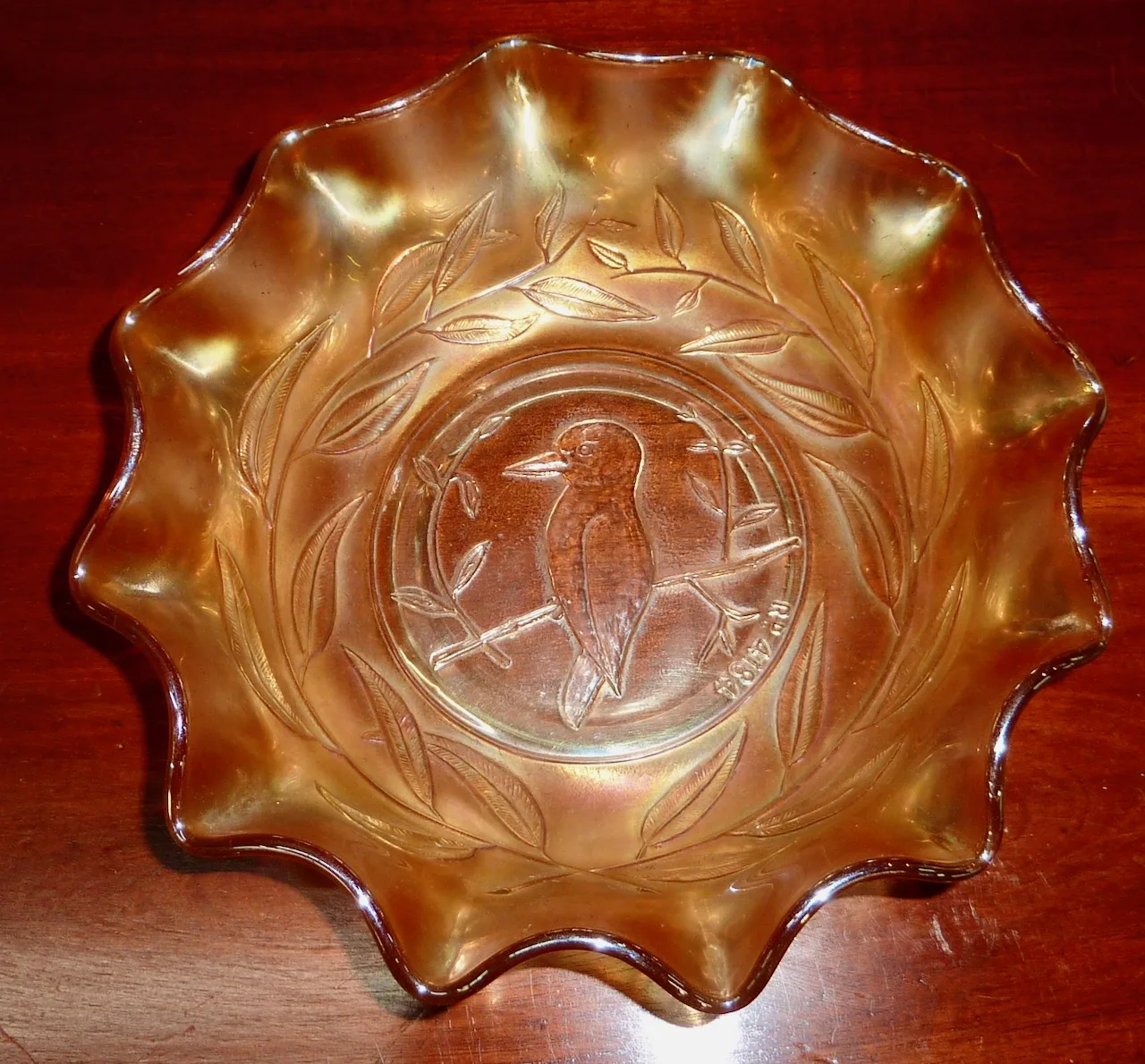 Carnival glass bowl photographed from directly above, its centre moulded with a kookaburra perched on a branch inside a ruffled rim