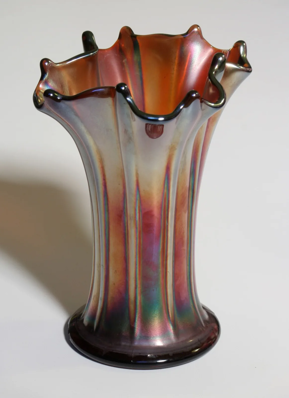 Tall carnival glass vase with vertical moulded ribs and a flared, pointed rim, its dark base glass showing purple and bronze iridescence
