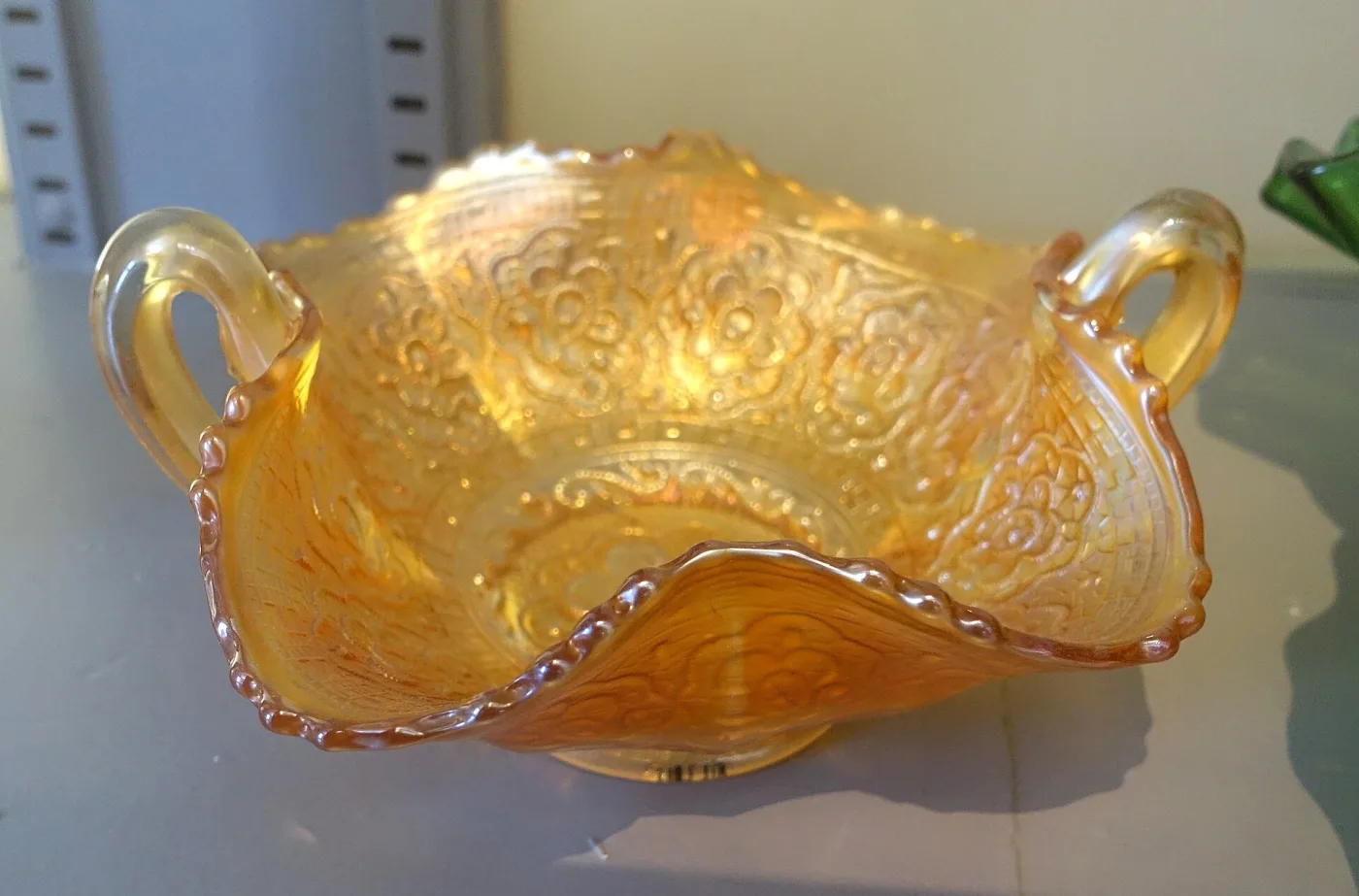 Shallow marigold carnival glass dish with a widely ruffled rim, in a museum case with a small printed label beside it