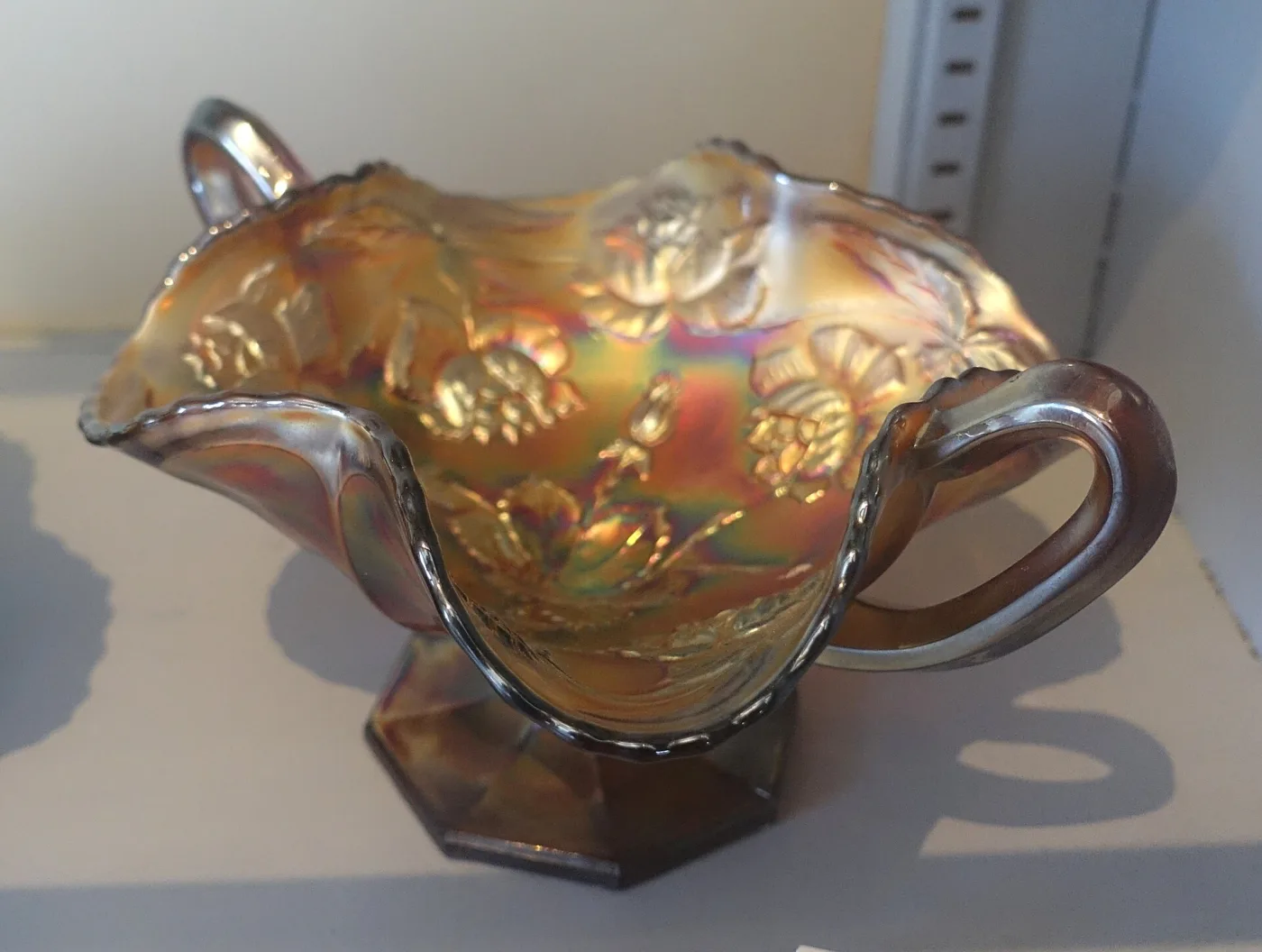 Footed marigold carnival glass dish with a ruffled rim and a moulded pattern, displayed in a museum case beside its accession card