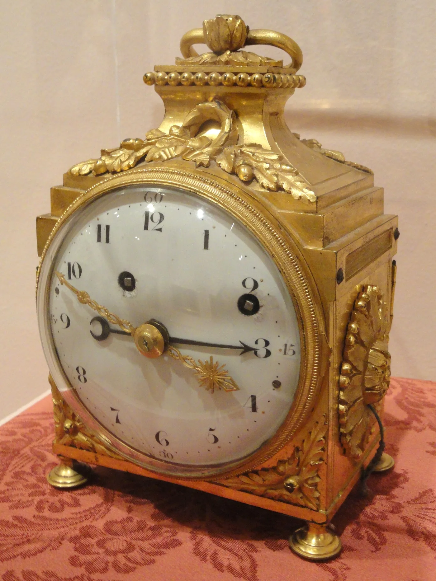 Gilt-bronze French travelling clock with a beaded top, oak-leaf mounts, a rigid carrying handle and a white dial with Arabic numerals