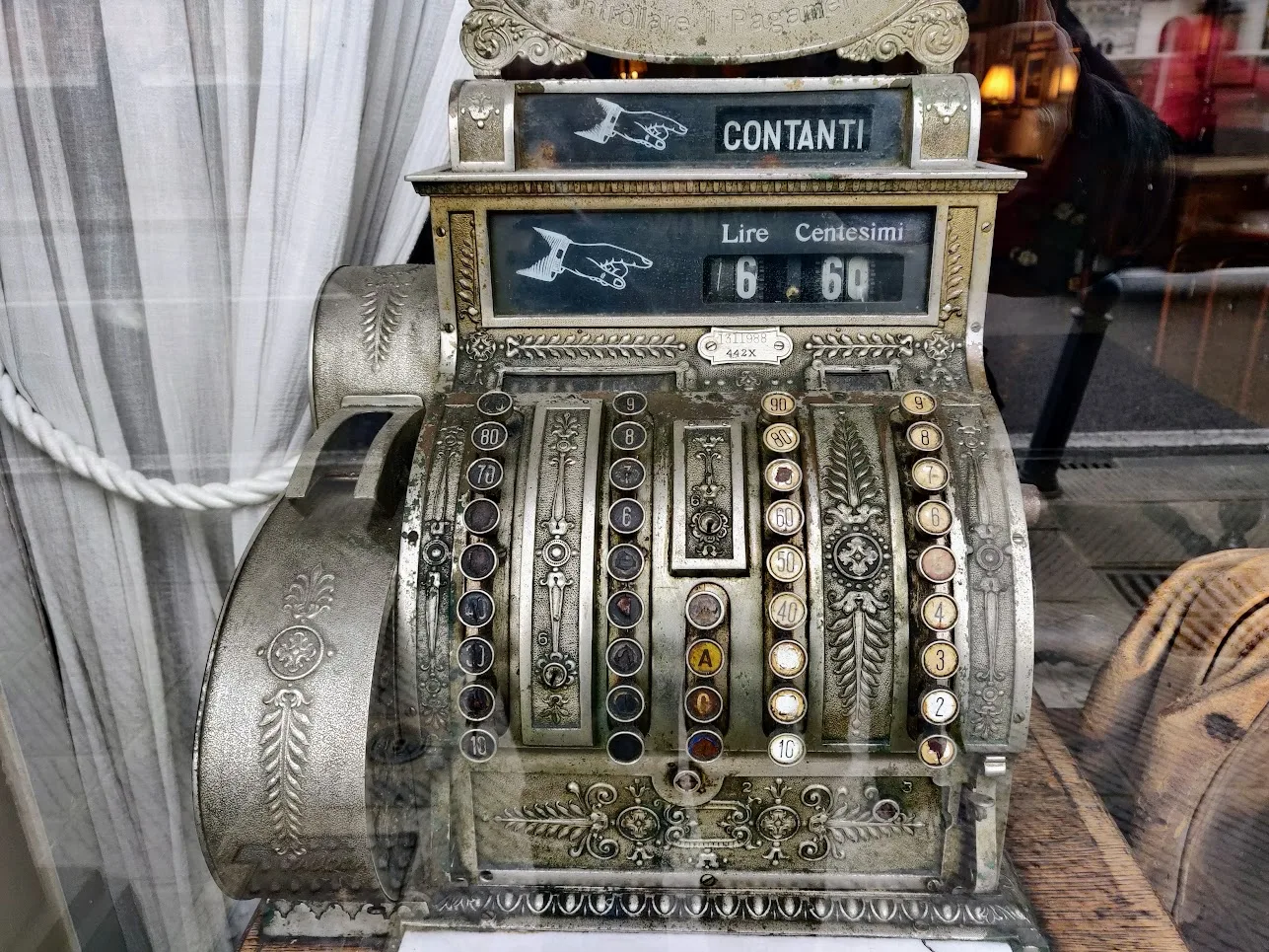 Nineteenth-century cash register with a glazed top sign reading contanti above a small amount card, standing in a hotel interior
