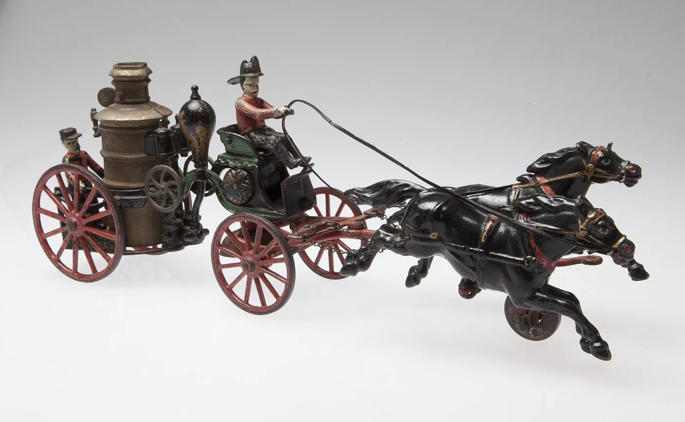 Cast iron toy fire engine drawn by two galloping black horses, with red spoked wheels, a nickel boiler and two seated figures, photographed against a plain ground