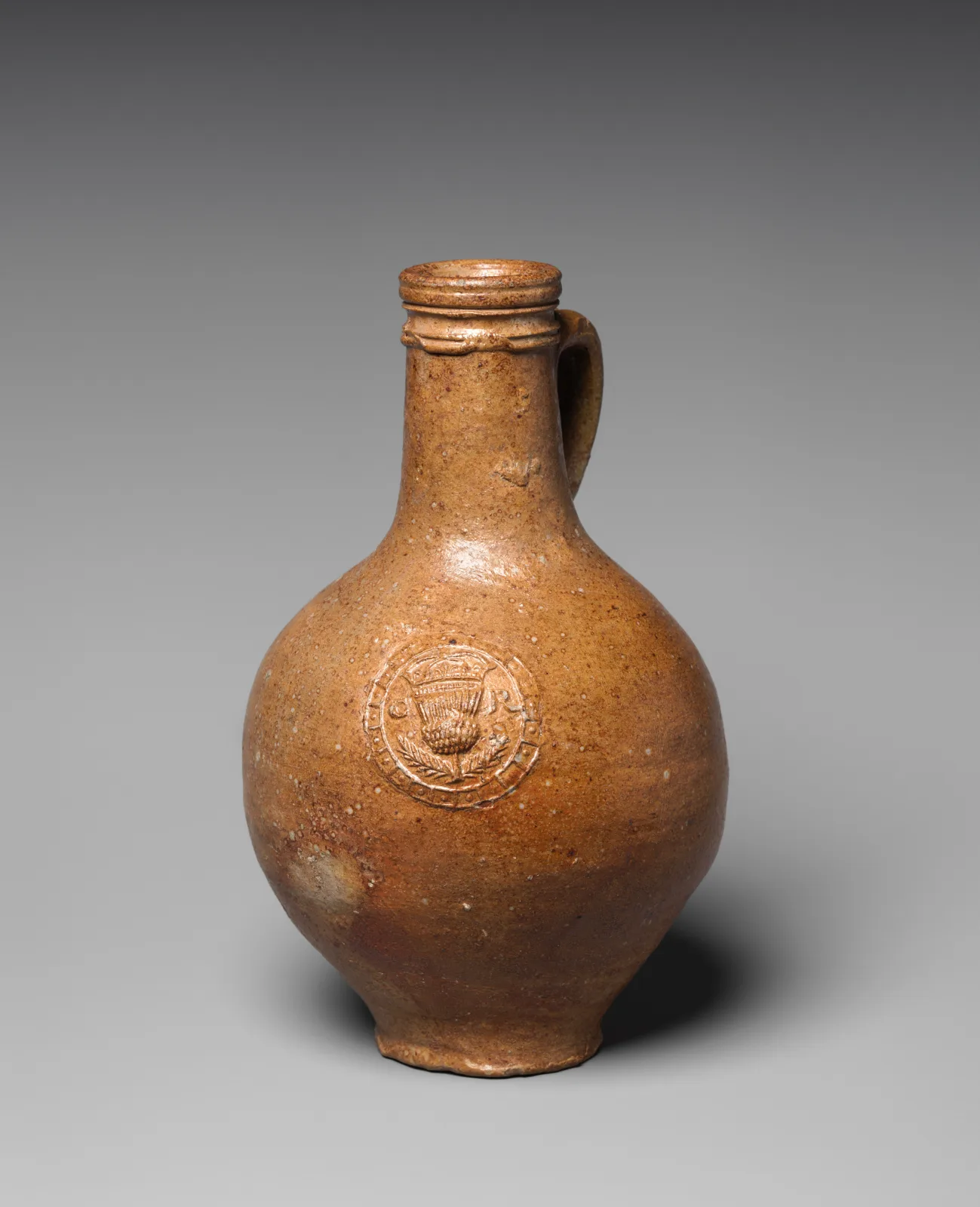 Small brown salt-glazed stoneware bottle with a loop handle and a round applied medallion stamped on the shoulder